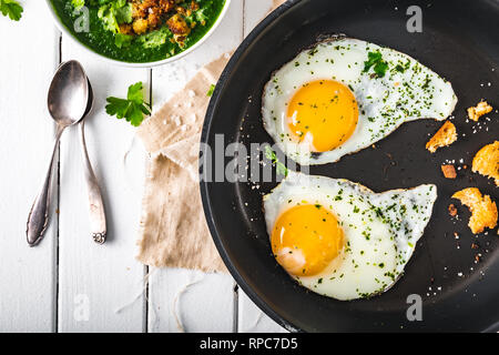 Zwei Spiegeleier in der Pfanne mit Kräutern und Salz für Spinat, Ansicht von oben Stockfoto