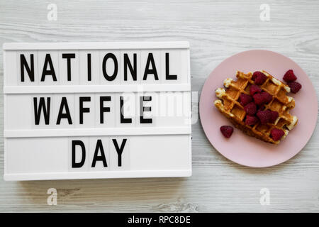 Lightbox mit Text "Nationalen Waffel Tag' und traditionelle belgische Waffeln mit Himbeeren auf Rosa die Platte über der weißen Holz- Oberfläche, Ansicht von oben. Stockfoto