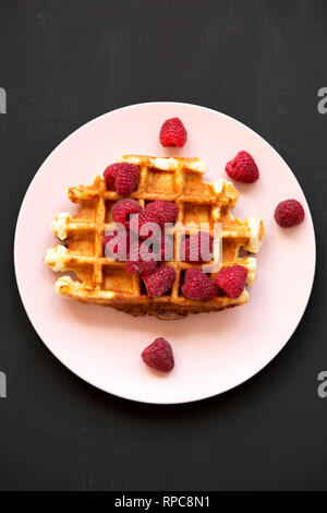Traditionelle belgische Waffeln mit Himbeeren auf rosa Platte über schwarze Oberfläche, Ansicht von oben. Flach, Overhead, von oben. Stockfoto