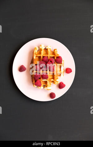 Traditionelle belgische Waffeln mit Himbeeren auf rosa Platte über schwarze Oberfläche, Ansicht von oben. Flach, Overhead, von oben. Stockfoto