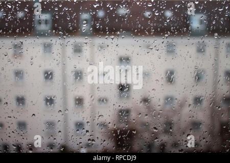 Tropfen Regen auf Glas, Regen fällt auf klares Fenster. Kondenswasser auf transparentem Glas über Stadt Landschaft oder ein Gebäude verwischen. Stockfoto