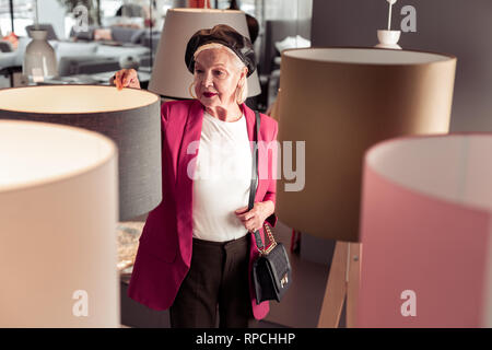 Stilvolle strahlende chic alternde Frau Auswahl torchere im Showroom Stockfoto