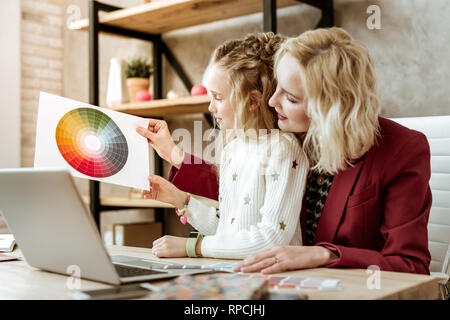 Neugierig inspiriert Langhaarigen kid Beobachtung Papier mit gedruckten Farbpalette Stockfoto