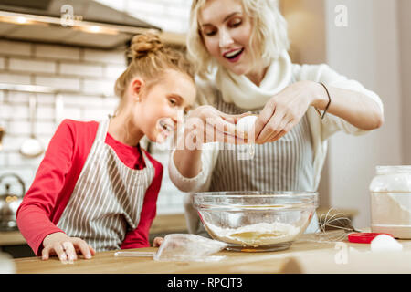 Fröhliche beteiligten Mutter zeigt trennen Eigelb vom Eiweiß Stockfoto