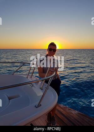 Portriat eines jungen normale Frau Yachtstewardess während des Sonnenuntergangs in der Stern eines super Boot im offenen Meer. Bahamas. Mit Sonnenbrille und lächelnd Stockfoto