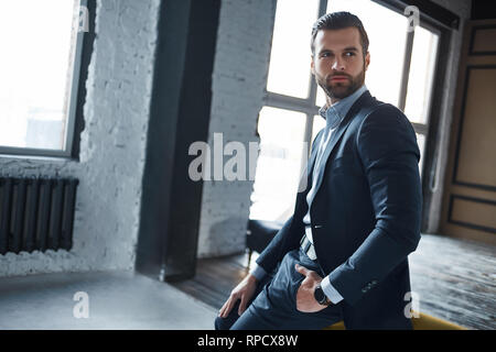 Portrait von Modern und stilvoll junger Geschäftsmann im Anzug, der ernsthaft zur Seite schaut, und denken Sie dabei an Arbeit. Business Konzept Stockfoto