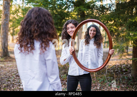 Fröhliche junge Frau, Reflexion der Zwillingsschwester im Herbst Tag im Wald Stockfoto