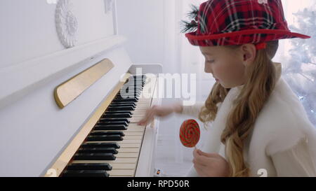 Funny Girl in Red hat Musik am Piano und Lutscher in der Hand halten Stockfoto