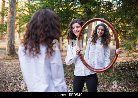 Fröhliche junge Frau, Reflexion der Zwillingsschwester im Herbst Tag im Wald Stockfoto