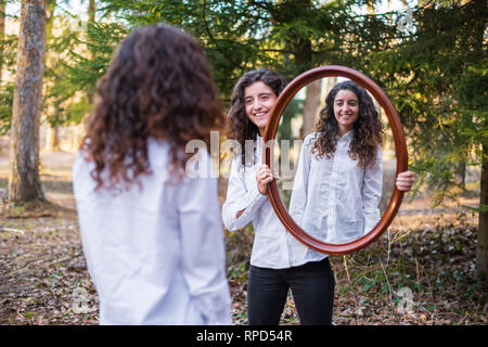 Fröhliche junge Frau, Reflexion der Zwillingsschwester im Herbst Tag im Wald Stockfoto