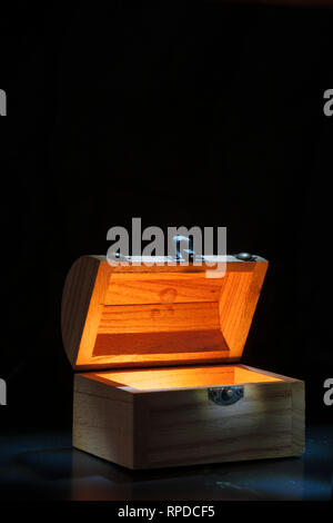 Kleine hölzerne Truhe im Inneren leuchtet vor einem schwarzen Hintergrund. Stockfoto