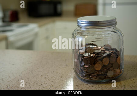 Glas Glas voller Münzen befindet sich auf Zähler gegen einen unscharfen Küche Hintergrund. Stockfoto