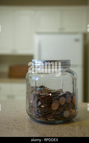 Glas Glas voller Münzen befindet sich auf Zähler gegen einen unscharfen Küche Hintergrund. Stockfoto