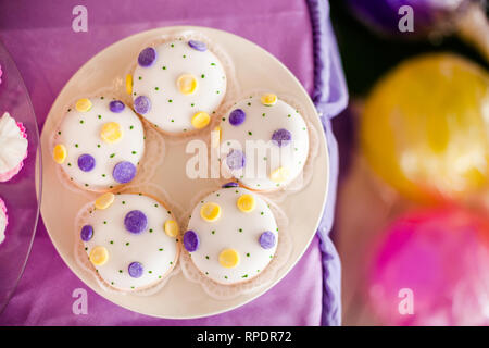 Candy Bar zum Geburtstag. Weiße, runde Kuchen mit großen gelben und violetten Punkten und mit kleinen grünen Punkte. Ansicht von oben Stockfoto