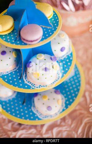 Candy Bar zum Geburtstag. Weiße, runde Kuchen mit großen gelben und violetten Punkten und mit kleinen grünen Punkte. Farben pink und lila Macarons. Ansicht von oben Stockfoto
