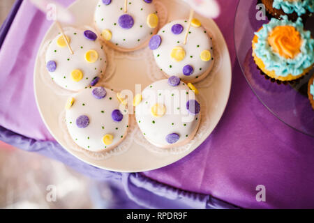 Candy Bar zum Geburtstag. Weiße, runde Kuchen mit großen gelben und violetten Punkten und mit kleinen grünen Punkte. Farben pink und lila Macarons. Ansicht von oben Stockfoto