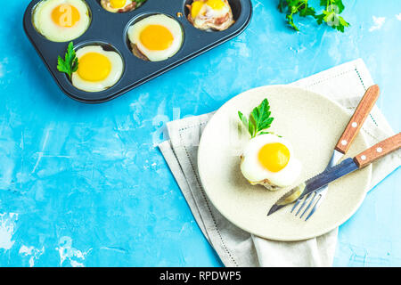 Gebackene Eier in der Licht- und Backformen. Portioniert Auflauf von Speck und Eier im italienischen Stil. Blauer Beton Tischfläche Hintergrund. Stockfoto