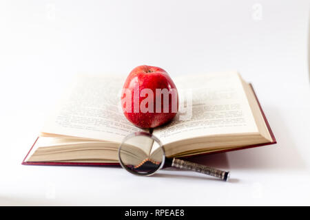Buch, Lupe und Apfel auf dem Tisch. Das Buch mit dem roten Apfel öffnen. Zum ersten Mal in der Schule. Grundschule. Stockfoto