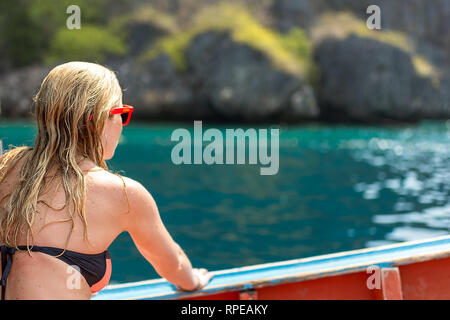 Eine blonde Frau in einem Bikini sitzt auf einem hölzernen Bootes genießen Sie die tropische Umgebung. Stockfoto