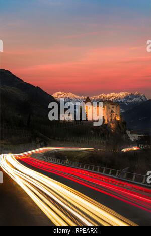Leichte Wanderwege auf der Straße vorbei an Schloss in Richtung Berge in Südtirol - Sonnenuntergang / alpine glow Stockfoto