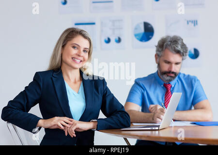 Schönen deutschen Geschäftsfrau mit blondem Haar und Computer am Schreibtisch im Büro der Firma Stockfoto