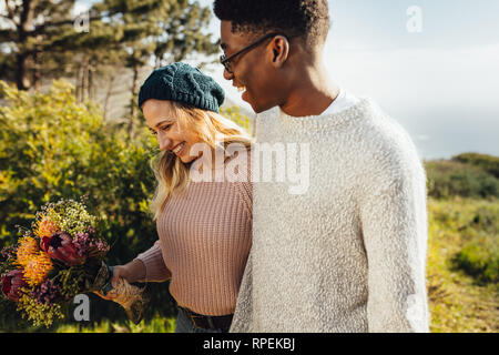 Lächelnde Frau mit Blume zu Fuß mit ihrem Freund im Freien. Paar in Liebe zusammen gehen im Freien. Stockfoto