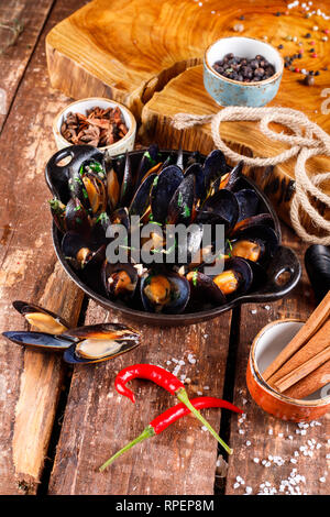 Gekochte Miesmuscheln in Kupfer Teller für Kochen auf Holz- hintergrund, in der Nähe von Seil und Produkte für die Küche close-up Stockfoto