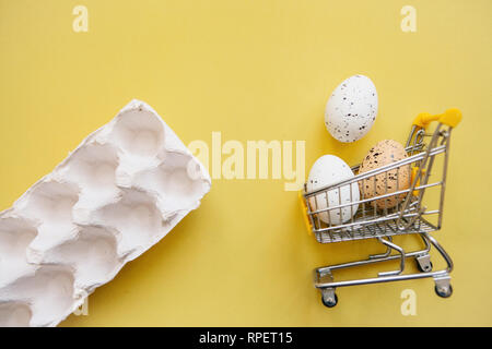 Warenkorb mit Eiern auf einem gelben Hintergrund. Das Konzept der Eine festliche Ostern Verkauf in einem minimalistischen Stil. Stockfoto