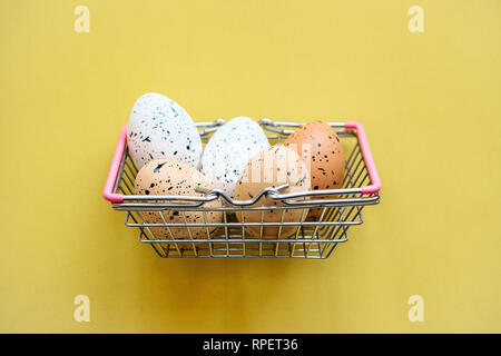 Korb mit Eiern auf einem gelben Hintergrund. Das Konzept der Eine festliche Ostern Verkauf in einem minimalistischen Stil. Stockfoto