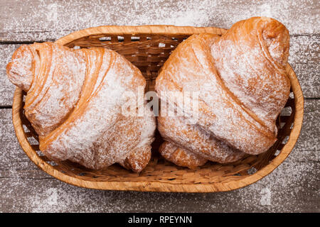 Zwei Croissants bestreut mit Puderzucker in einem Weidenkorb auf alten Holz- Board Ansicht von Oben Stockfoto