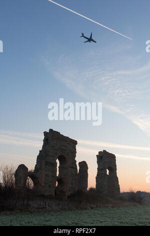 Rom - die Ruinen eines Aquädukts mit einem Flugzeug über ihm fliegen in den frühen Morgen im Parco degli Acquedotti. Stockfoto