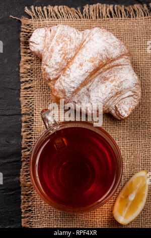 Croissant mit einer Tasse Tee auf einen Sack. Ansicht von oben Stockfoto