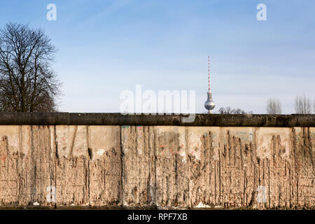 Berliner Mauer original verwitterten Abschnitt mit freiliegenden Bügeleisen Bars zum Teil für den Fernsehturm (Berliner Fernsehturm) weit in den Horizont beschädigt. Stockfoto