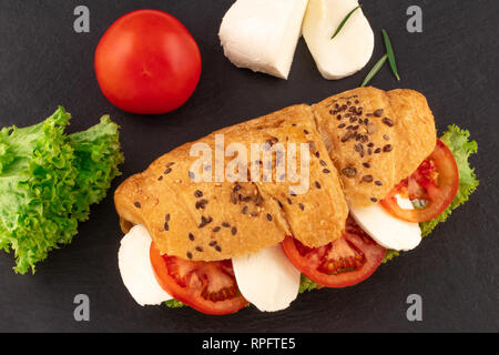 Croissant Sandwich mit Salat Mozzarella und Tomaten über schwarzen Stein. Gesunden Snack. Ansicht von oben. Stockfoto