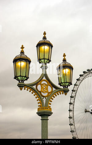 Verzierte dreiköpfige Gusseisenlaterne mit Gaslampen an der Westminster Bridge England London mit dem Londoner Auge im Hintergrund Stockfoto