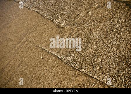 Meer Wasser macht undulating abstrakte Muster und Formen bei strahlendem Sonnenschein, wie es plätschert und wäscht über einen Sandstrand Stockfoto