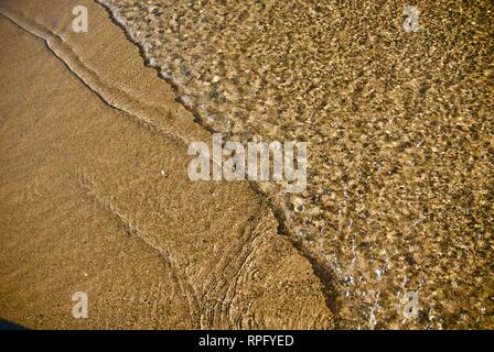 Meer Wasser macht undulating abstrakte Muster und Formen bei strahlendem Sonnenschein, wie es plätschert und wäscht über einen Sandstrand Stockfoto