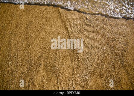 Meer Wasser macht undulating abstrakte Muster und Formen bei strahlendem Sonnenschein, wie es plätschert und wäscht über einen Sandstrand Stockfoto