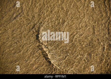 Meer Wasser macht undulating abstrakte Muster und Formen bei strahlendem Sonnenschein, wie es plätschert und wäscht über einen Sandstrand Stockfoto