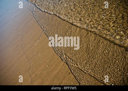 Meer Wasser macht undulating abstrakte Muster und Formen bei strahlendem Sonnenschein, wie es plätschert und wäscht über einen Sandstrand Stockfoto