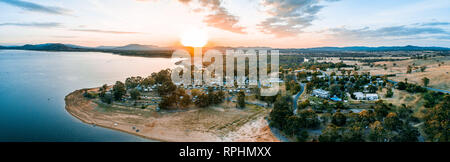 Sun Berühren der Horizont über Berge und Lake Hume Dorf - große Antenne panorama Stockfoto