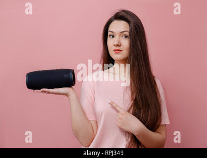 Glückliche junge attraktive Frau auf rosa Hintergrund Halten in der Hand tragbare Lautsprecher, um Musik zu hören Stockfoto