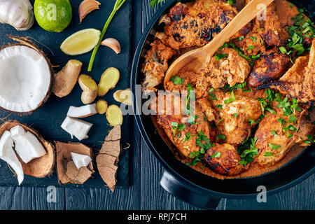 Kuku Paka, kenianische Spezialitäten vom Holzkohlegrill Huhn geschmort in cremiger würziger Kokosnuss Sauce aus Steingut Topf auf einem Holztisch. Zutaten auf einem Stein cu Stockfoto