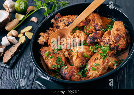 Kuku Paka, kenianische Spezialitäten vom Holzkohlegrill Huhn geschmort in cremiger würziger Kokosnuss Sauce aus Steingut Topf auf einem Holztisch. Zutaten auf einem Stein cu Stockfoto