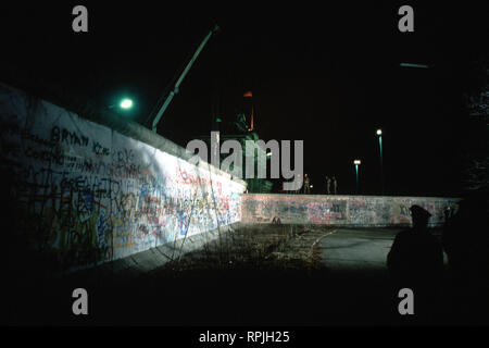 Ostdeutsche Wachen beobachten, wie ein Kran bereitet einen Abschnitt der Berliner Mauer am Brandenburger Tor zu entfernen. Stockfoto