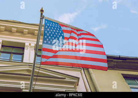 Riga, Lettland. Usa Amerika Flagge in der Nähe des Gebäudes. Sonnigen und kalten Tag. Urban reisen Foto 2019. Am 21. Februar . Stockfoto