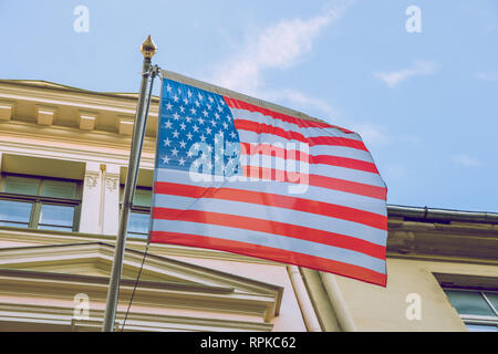 Riga, Lettland. Usa Amerika Flagge in der Nähe des Gebäudes. Sonnigen und kalten Tag. Urban reisen Foto 2019. Am 21. Februar . Stockfoto