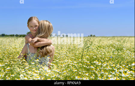 Süße kleine Mädchen umarmte ihre Mutter auf der blühenden Wiese, blauen Himmel im Hintergrund Stockfoto