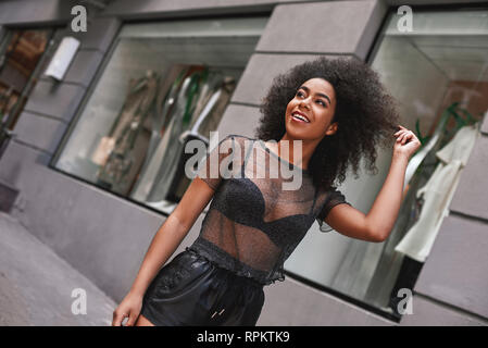 Unglaublich schön. Schöne afro-amerikanische Frau in Leder Hosen das Spielen mit ihrem Haar, während auf der Straße. Fashion Look Stockfoto