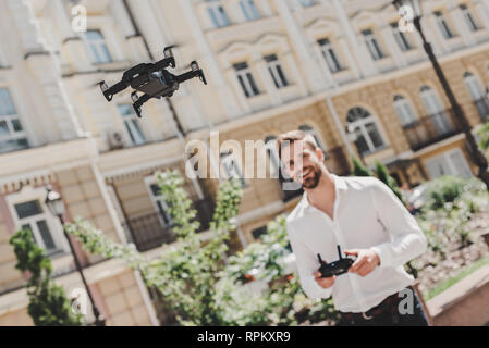 Hübscher junger Geschäftsmann zu Fuß auf der Straße der Stadt, die Drohne, smart casual Outfit tragen Jeans und weißem T-Shirt. Urban lifestyle junger Fachleute. Stockfoto
